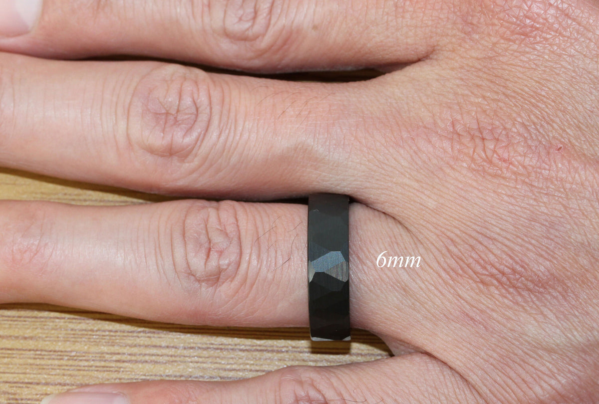 May include: A black ring with a hammered finish, worn on a finger. The ring is 6mm wide.
