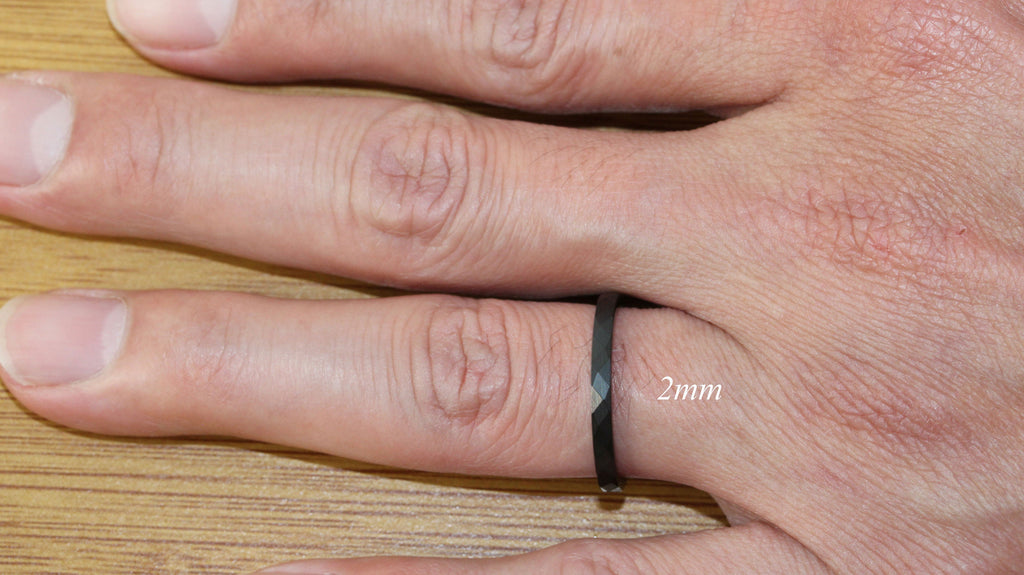 May include: A black ring with a diamond-shaped design on a finger. The ring is 2mm wide.