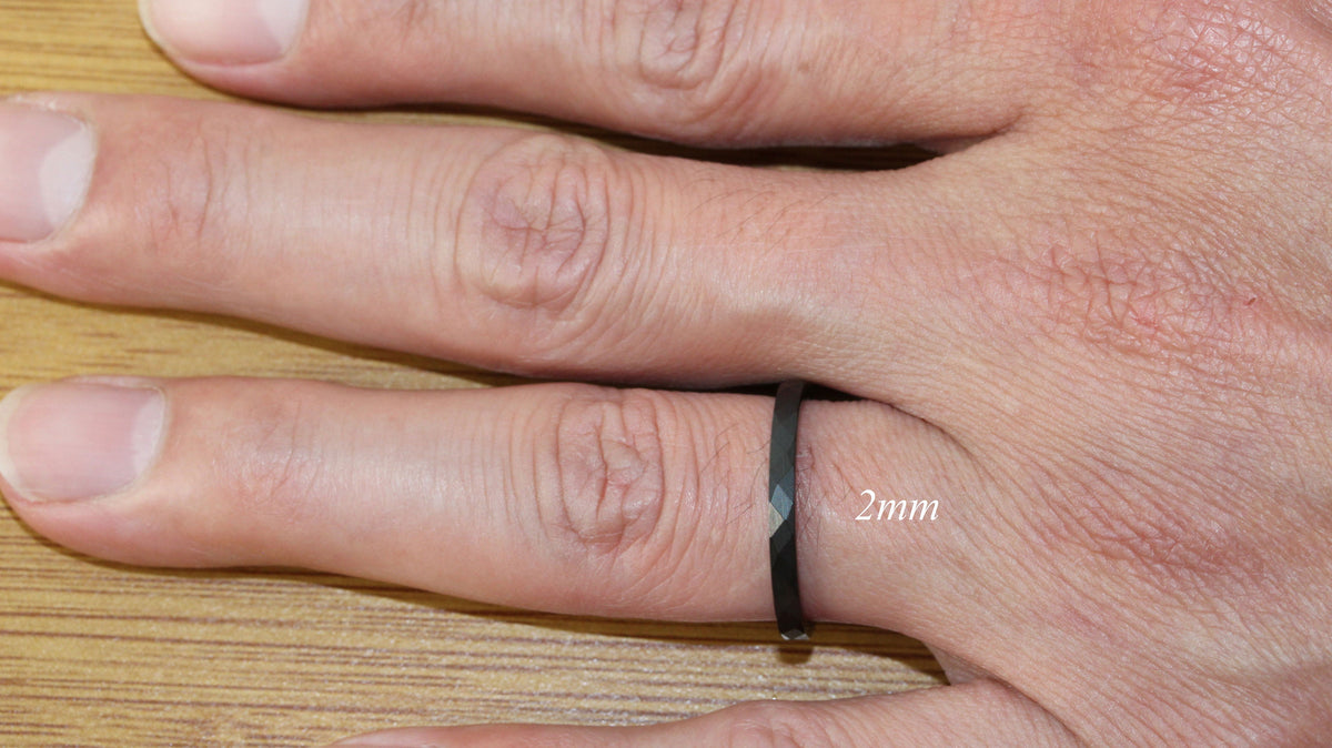 May include: A black ring with a diamond-shaped design on a finger. The ring is 2mm wide.