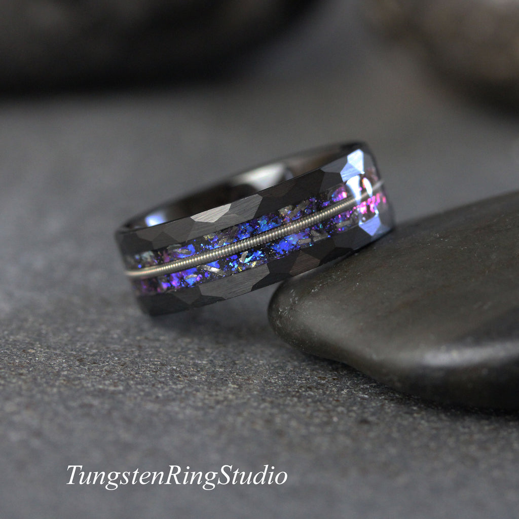 May include: Black tungsten carbide ring with a hammered finish and a blue and purple iridescent inlay. The ring has a thin silver band running through the center.