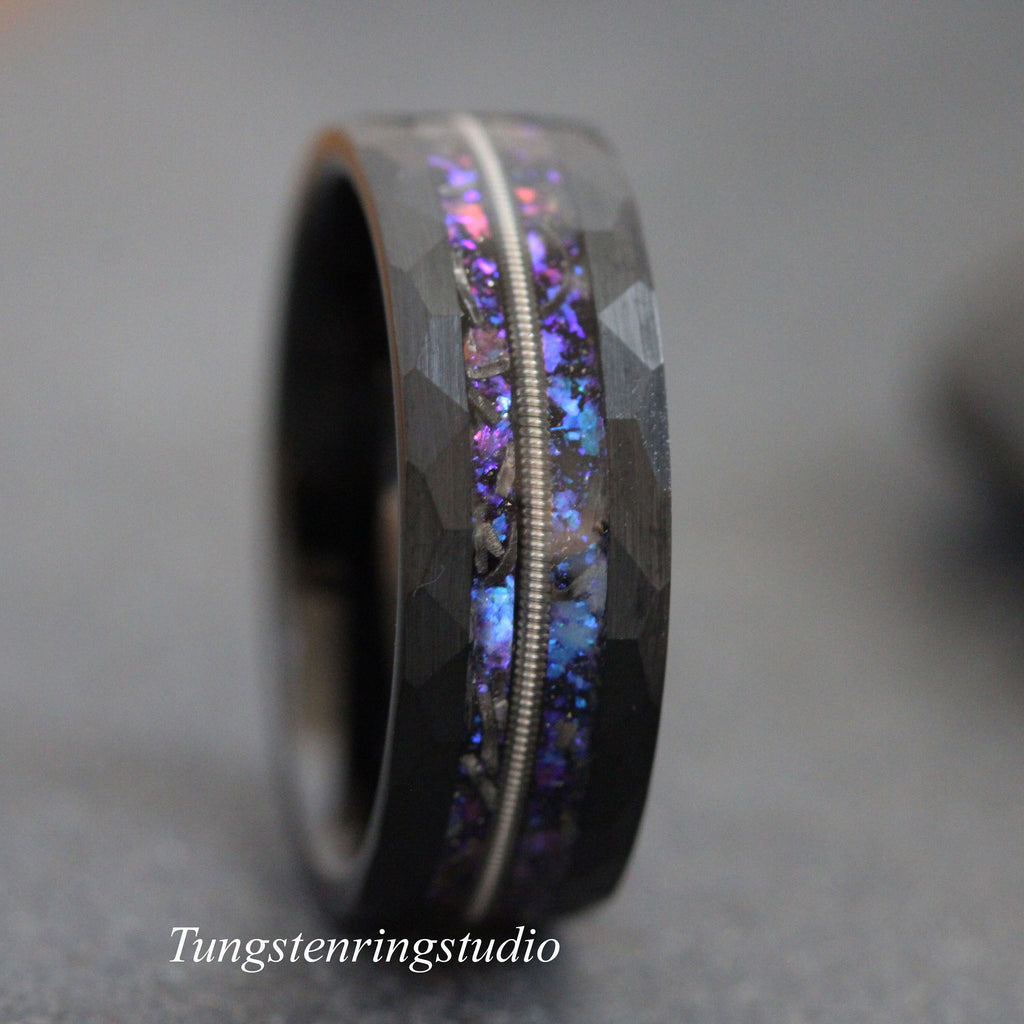 May include: A black tungsten carbide ring with a hammered finish and a thin silver inlay. The inlay is filled with iridescent blue and purple glitter.