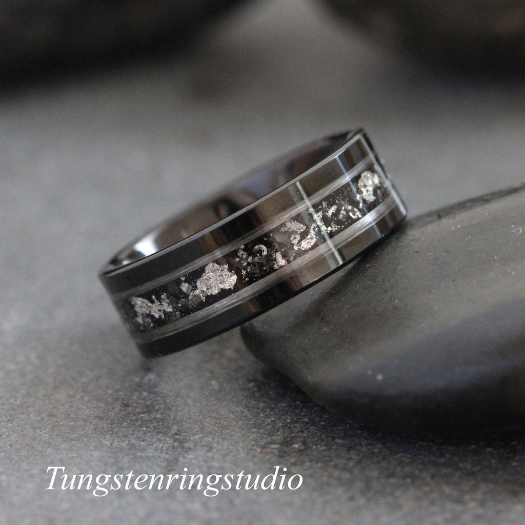 May include: A black tungsten carbide ring with a silver inlay. The inlay has a scattered pattern of small silver pieces.