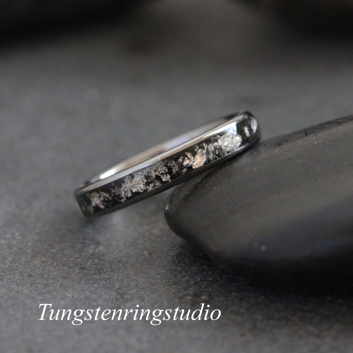 May include: A black tungsten carbide ring with a silver inlay. The ring is on a gray background.