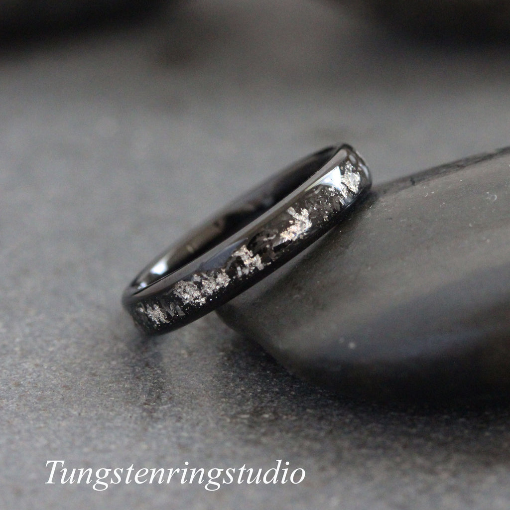 May include: A black tungsten carbide ring with a silver inlay design. The ring is on a dark gray background.