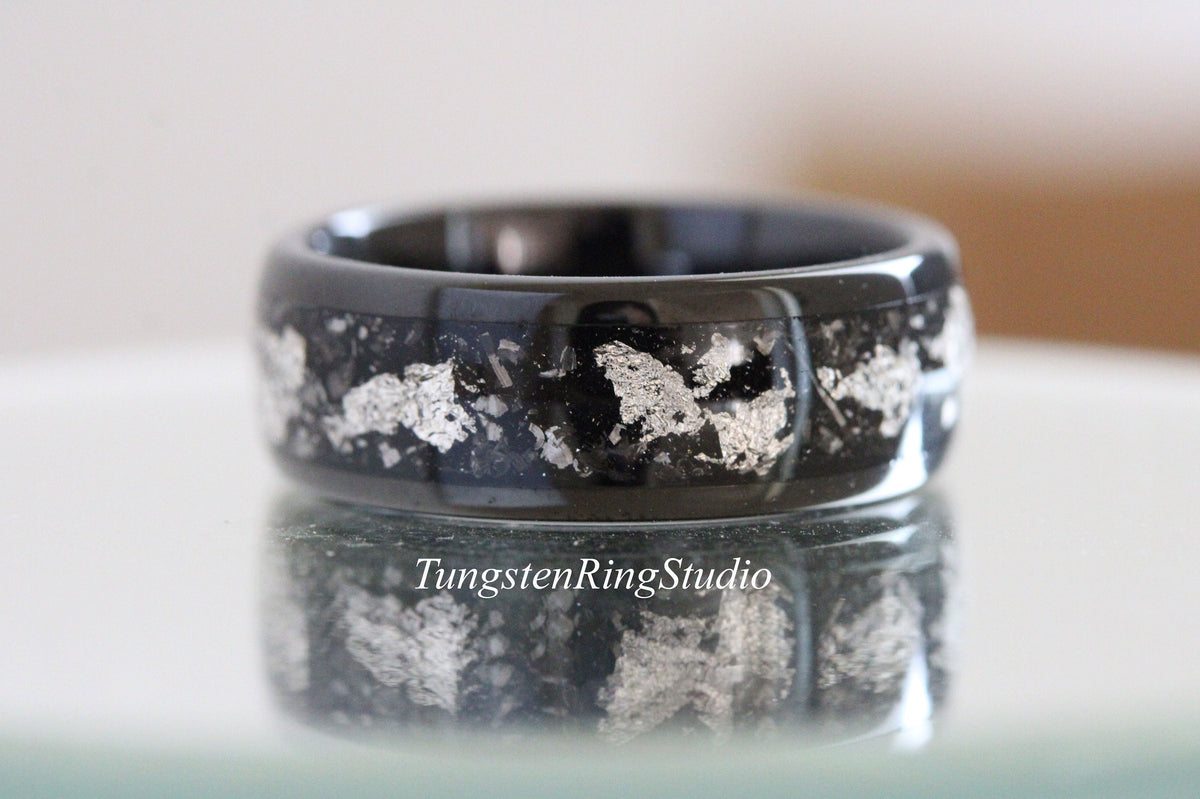 May include: Black tungsten carbide ring with silver flakes embedded in the band. The ring is polished and has a smooth finish.