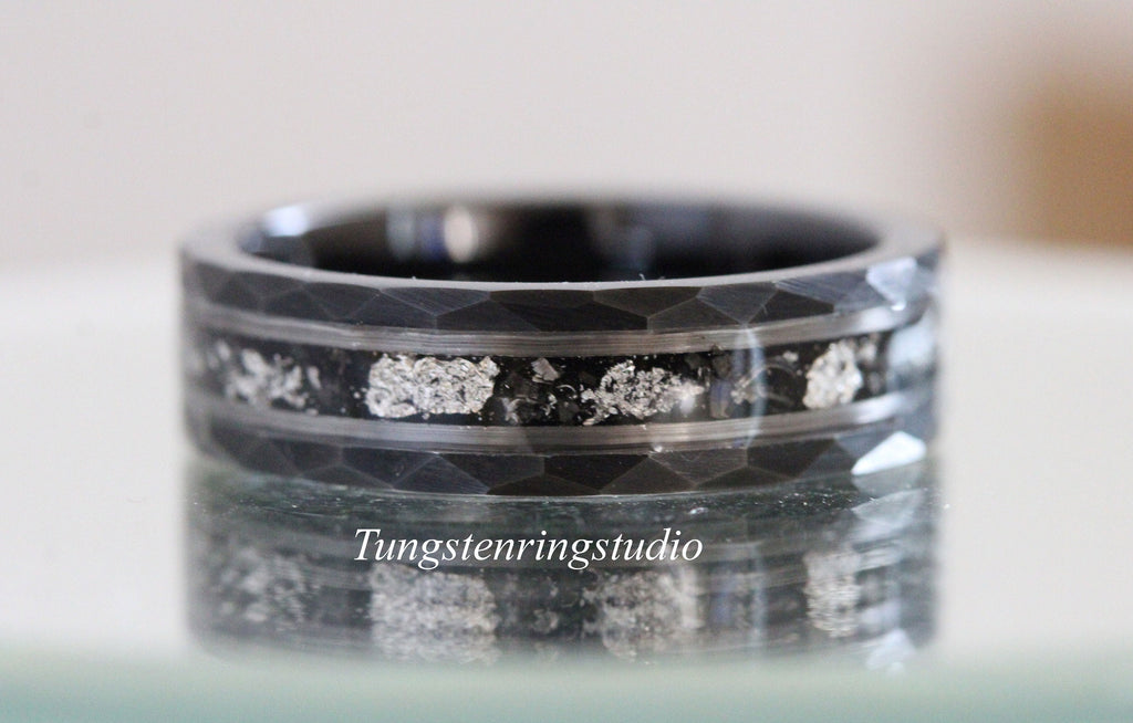 May include: A black tungsten carbide ring with a hammered finish and a silver inlay. The inlay is made of silver particles embedded in the ring.