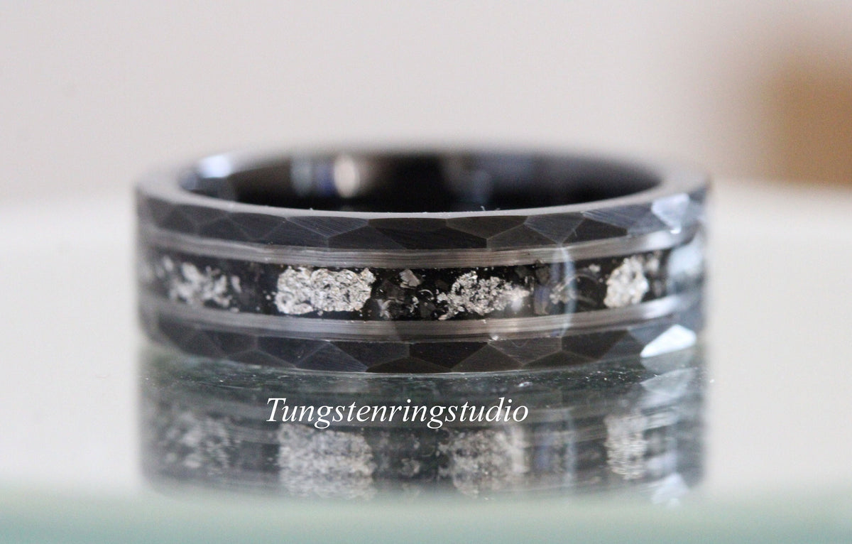 May include: A black tungsten carbide ring with a hammered finish and a silver inlay. The inlay is made of silver particles embedded in the ring.