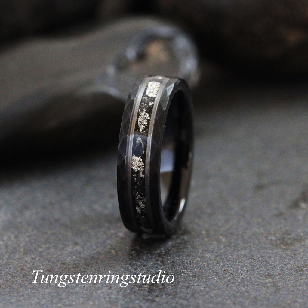 May include: A black tungsten carbide ring with a hammered finish and a silver inlay. The inlay features a pattern of small silver dots.