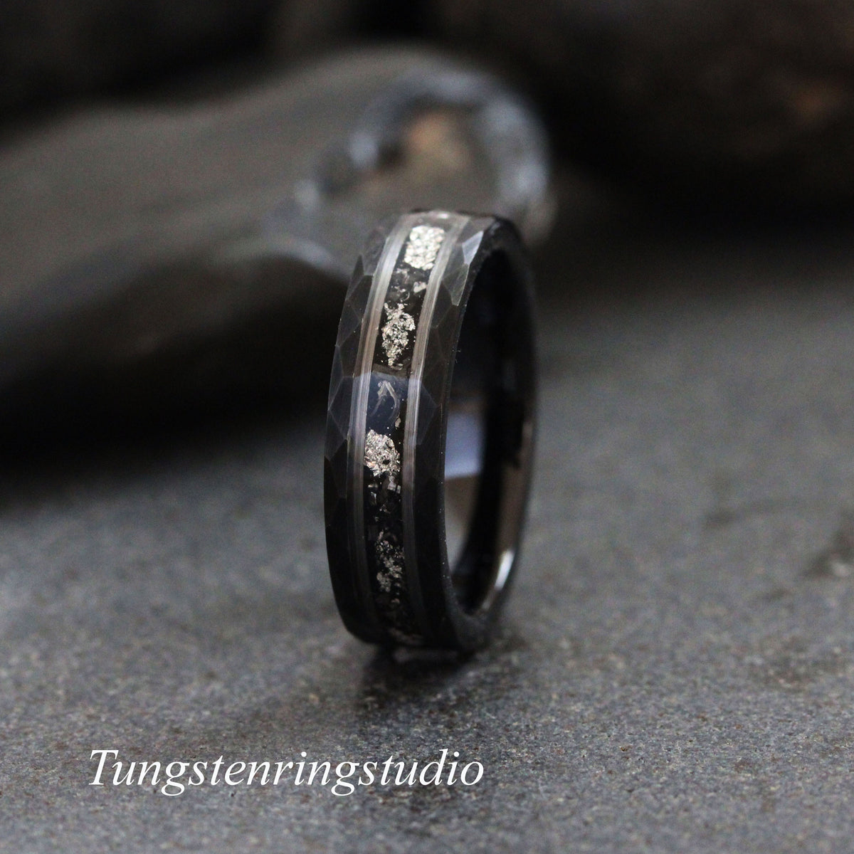May include: A black tungsten carbide ring with a hammered finish and a silver inlay. The inlay features a pattern of small silver dots.