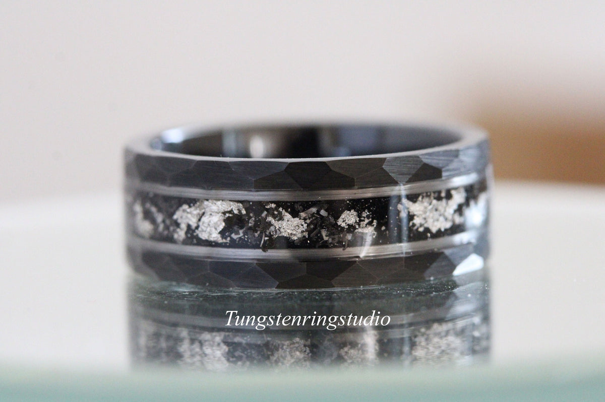 May include: A black tungsten carbide ring with a hammered finish and silver inlay. The ring has a wide band and a polished edge.