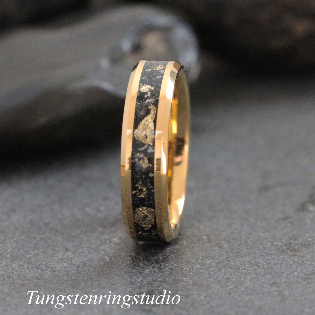 May include: A gold-colored ring with a black inlay speckled with gold-colored flakes. The ring has a polished finish and the text "Tungstenringstudio" is at the bottom of the image. This ring is a piece of jewelry.