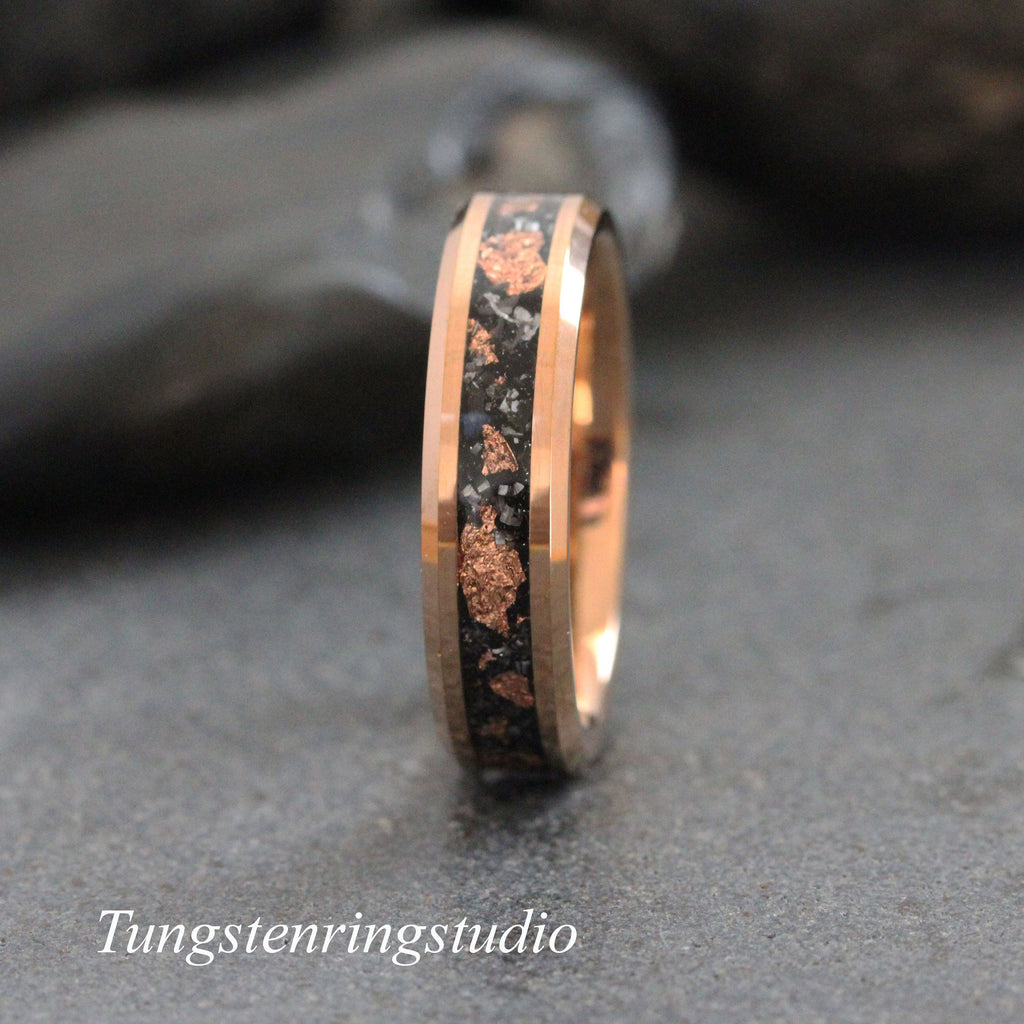 May include: A tungsten carbide ring with a black and rose gold inlay. The inlay features a pattern of small, irregular shapes.