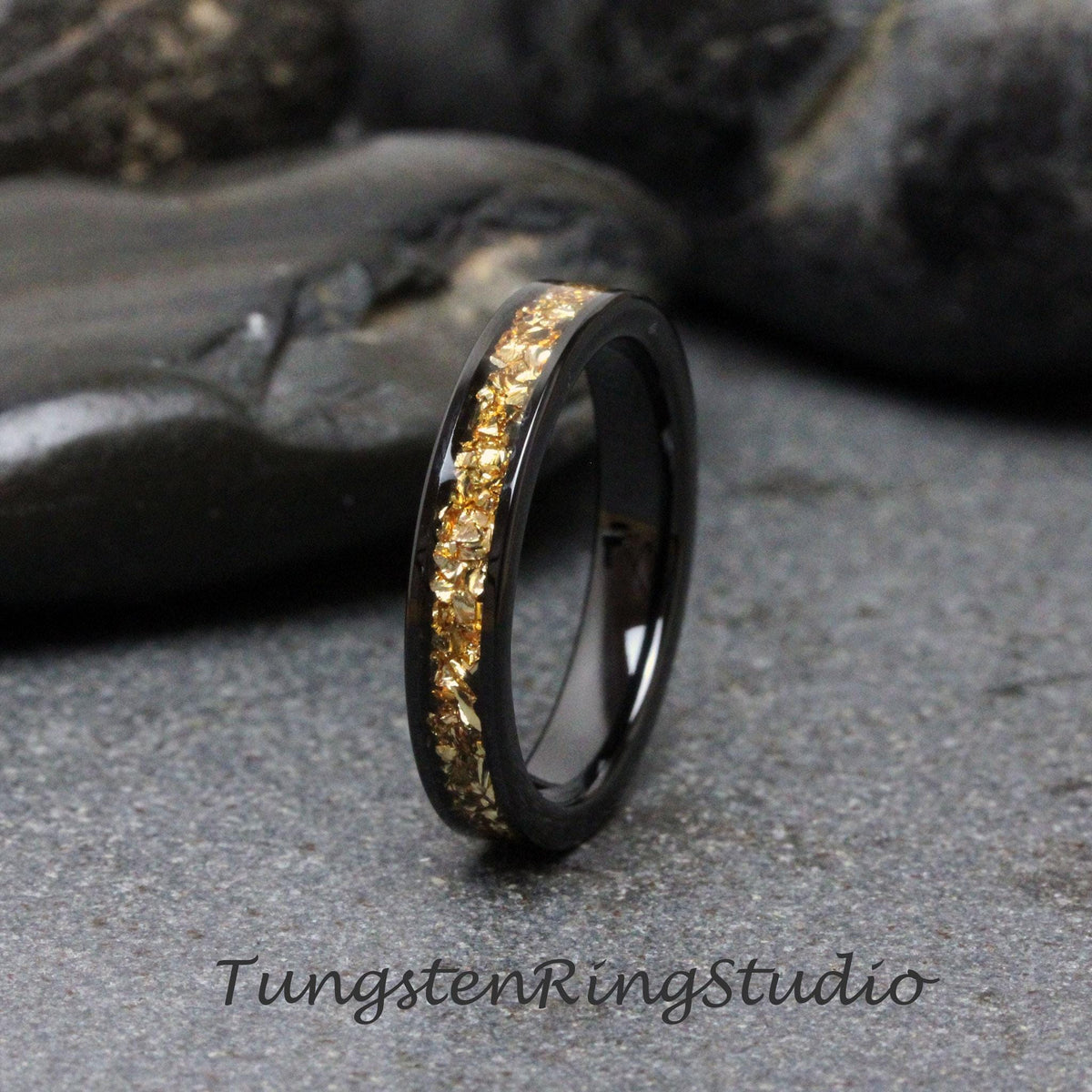 May include: A black tungsten carbide ring with a gold inlay. The inlay is a band of gold flakes that wraps around the ring.