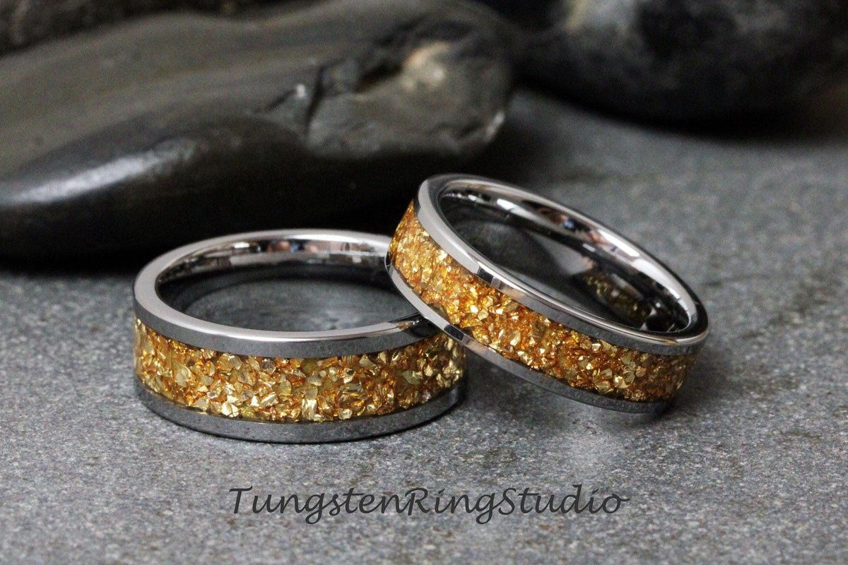May include: Two silver tungsten carbide rings with a gold inlay. The inlay is made of small gold particles.