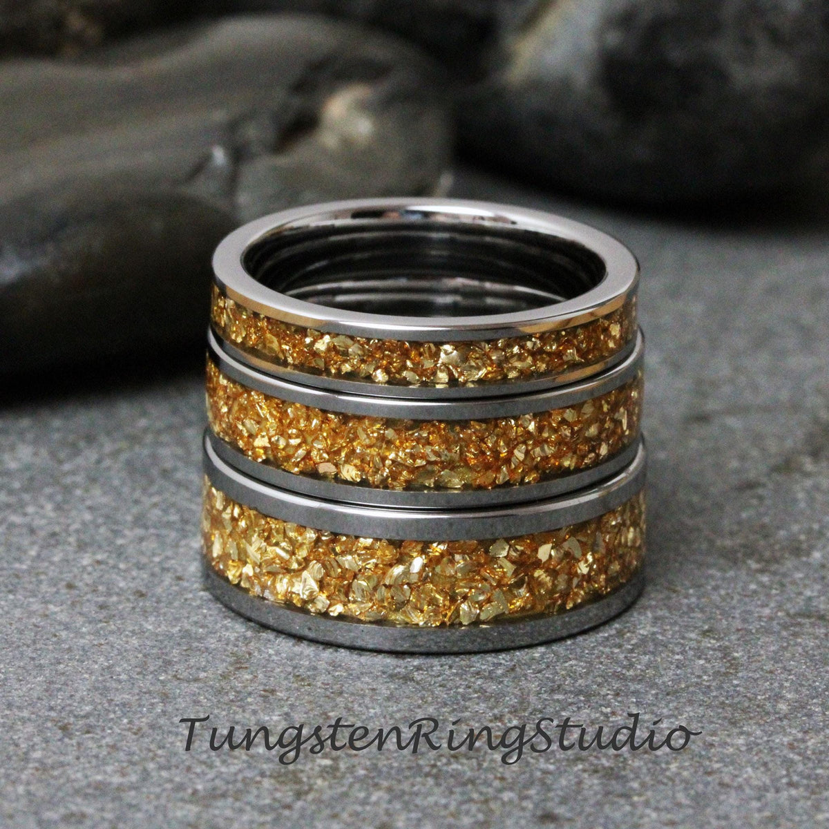 May include: Three stacked tungsten rings with a gold inlay. The rings are a silver color with a gold fleck design.