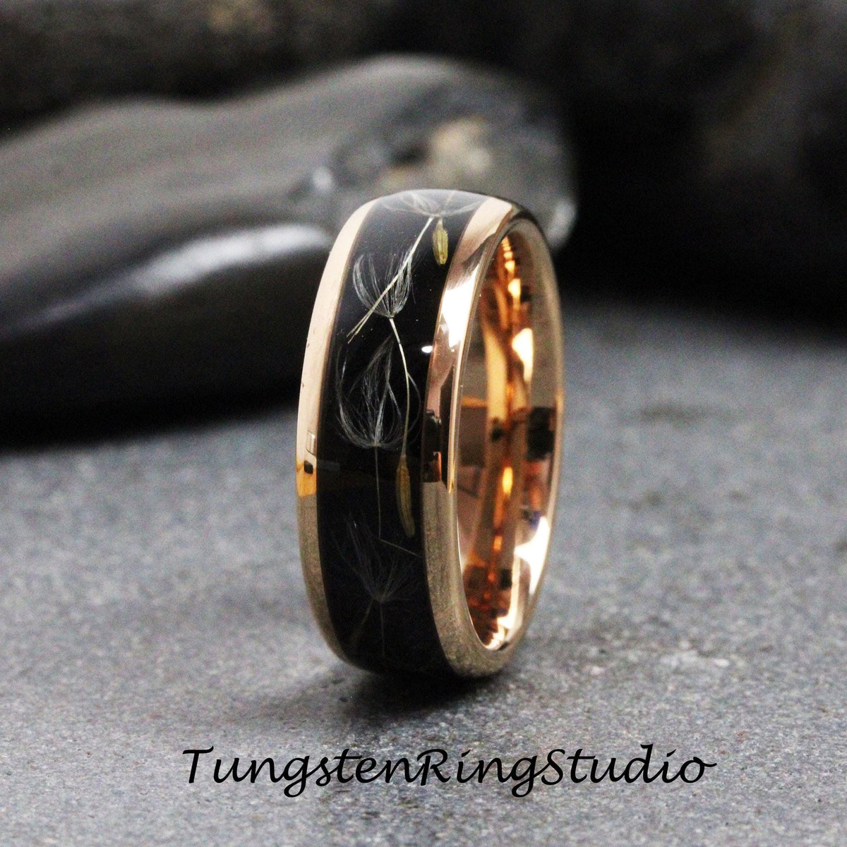 May include: A black tungsten ring with a rose gold band and a design of dandelion seeds embedded in the black surface.