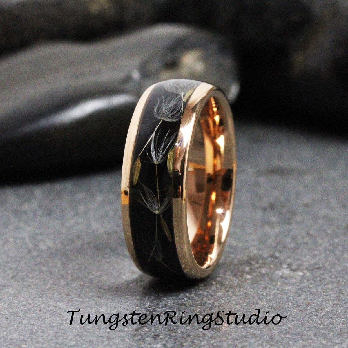 May include: A black tungsten ring with a rose gold band and a design of dandelion seeds embedded in the black band.