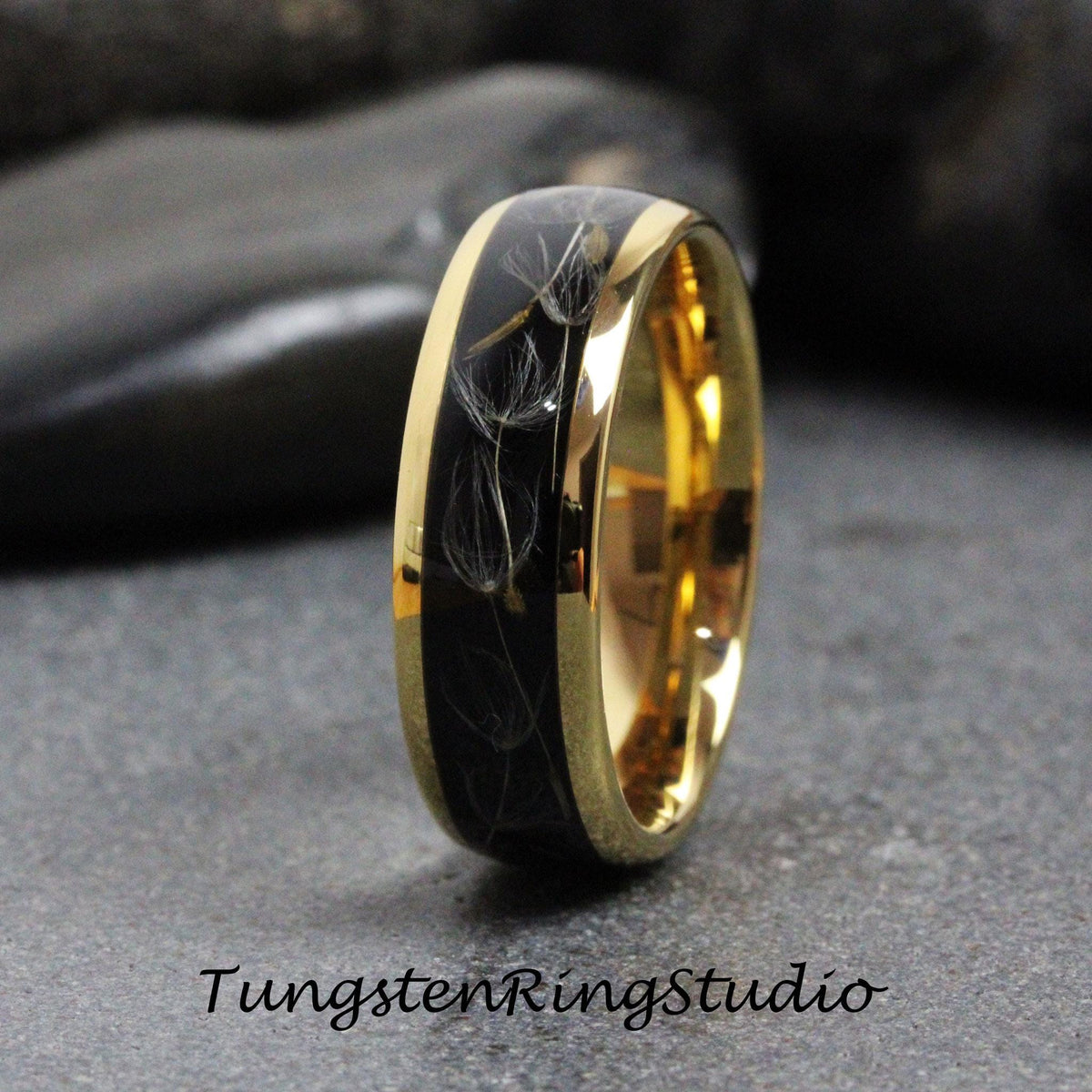 May include: A black tungsten ring with a gold band and a dandelion design. The ring is a wedding band.