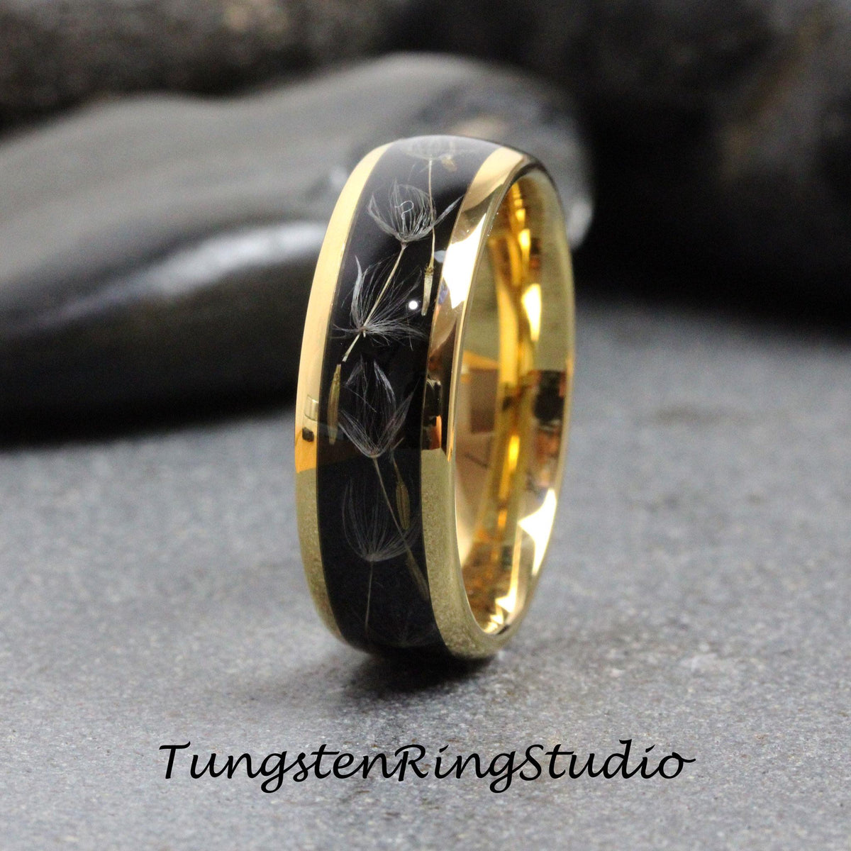 May include: A black tungsten ring with a gold band and a design of dandelion seeds embedded in the black surface.