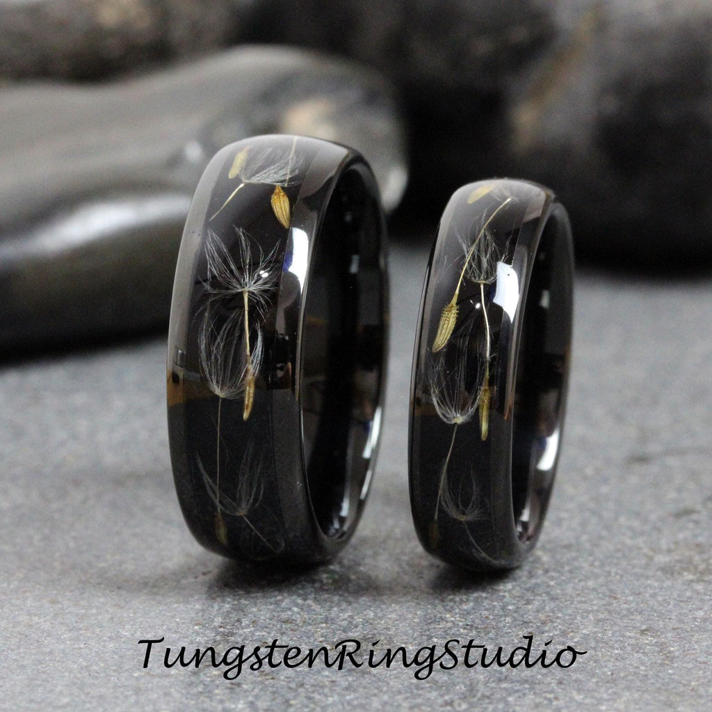 May include: Two black tungsten carbide rings with a dandelion design embedded in the band. The rings are polished and have a high shine.
