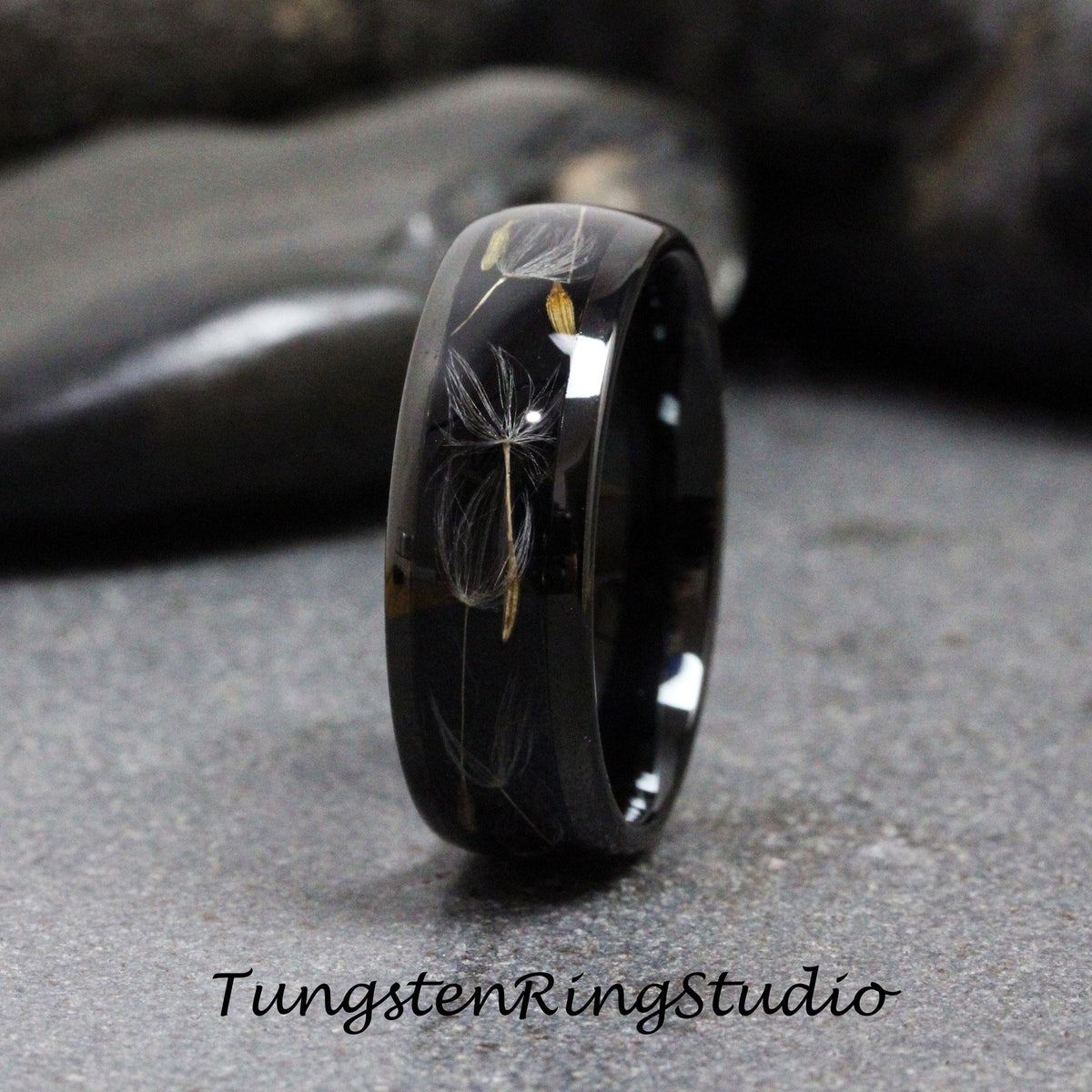 May include: A black tungsten ring with a dandelion seed design embedded in the band. The ring is polished and has a smooth finish.