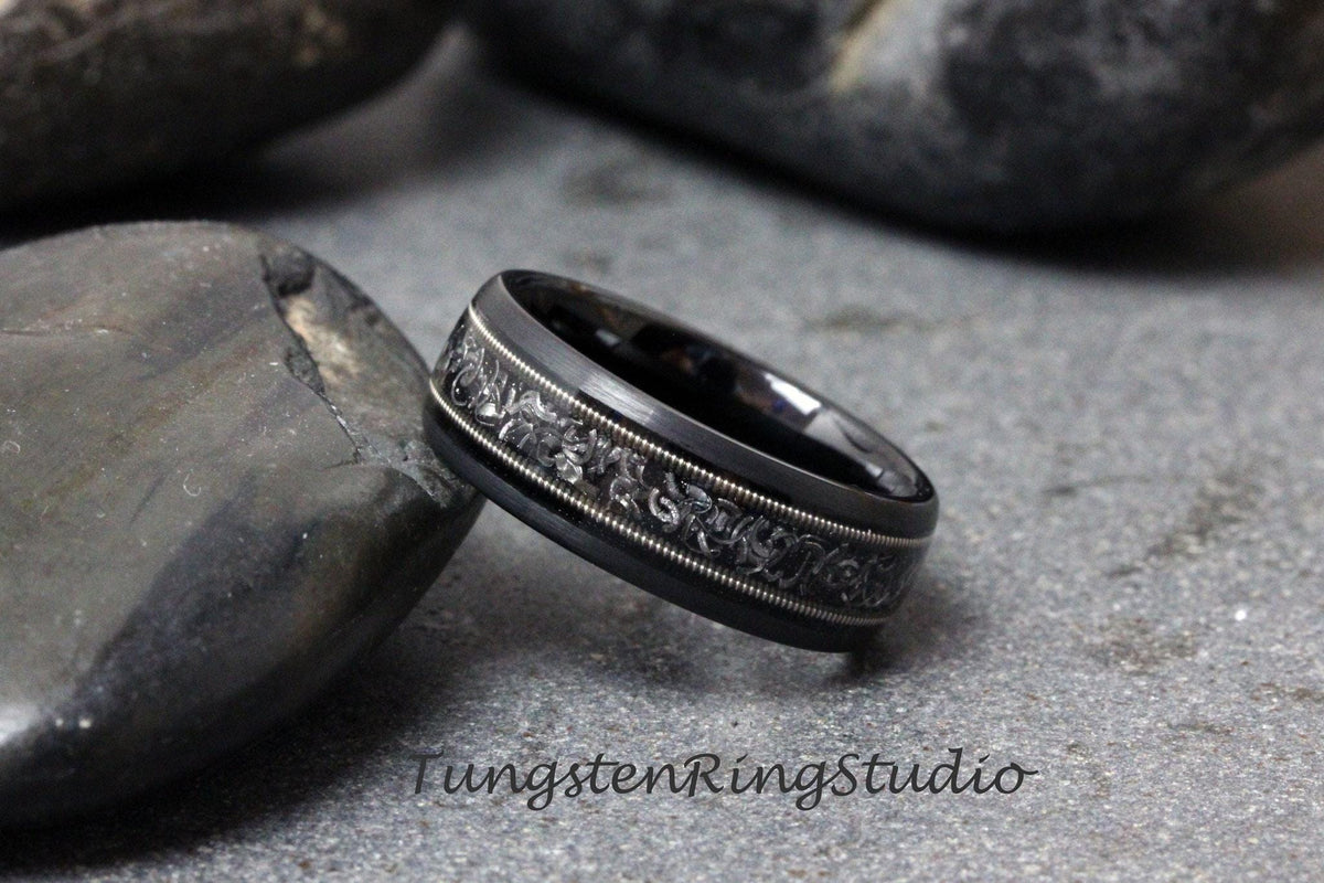 May include: A black tungsten carbide ring with a silver-colored band and an intricate engraved design.