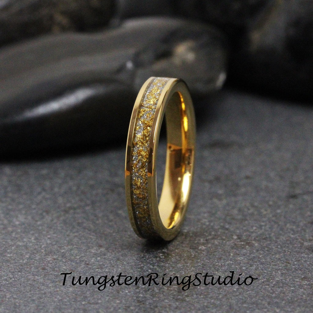 May include: A gold-colored ring with a band of gold and silver flecks. The ring has a polished finish and the text "TungstenRingStudio" is at the bottom. The ring is on a dark gray surface.