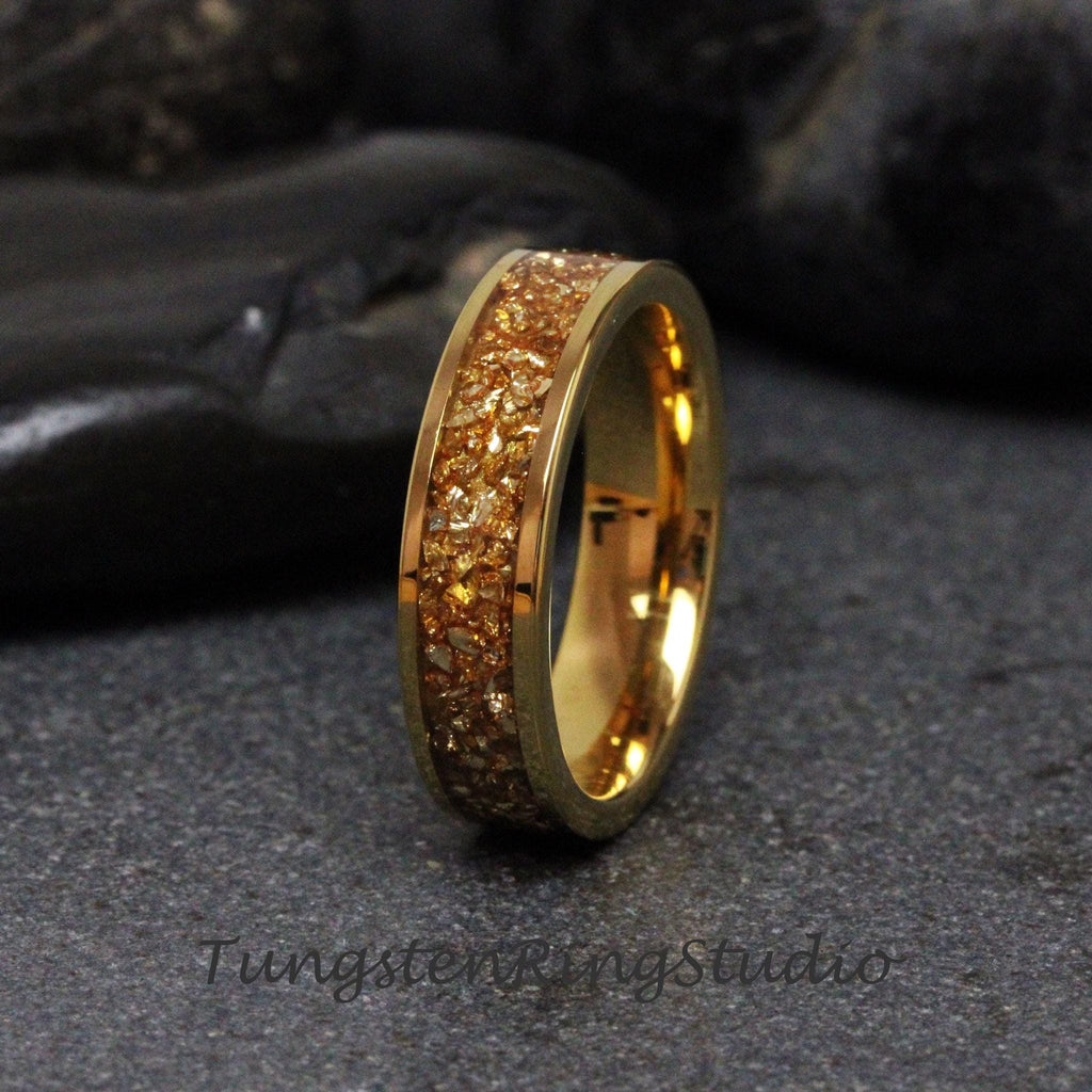 May include: A gold tungsten carbide ring with a band of embedded gold glitter. The ring is a simple design with a smooth, polished finish.