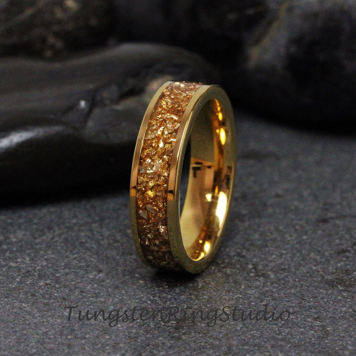 May include: A gold tungsten carbide ring with a band of embedded gold glitter. The ring is a simple design with a smooth, polished finish.