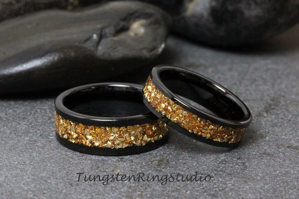 May include: Two black tungsten carbide rings with a gold inlay. The rings are on a gray surface.