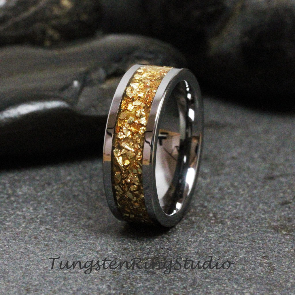 May include: A tungsten carbide ring with a gold inlay. The inlay is made of small gold flakes that are embedded in the ring. The ring is a classic style with a polished finish.
