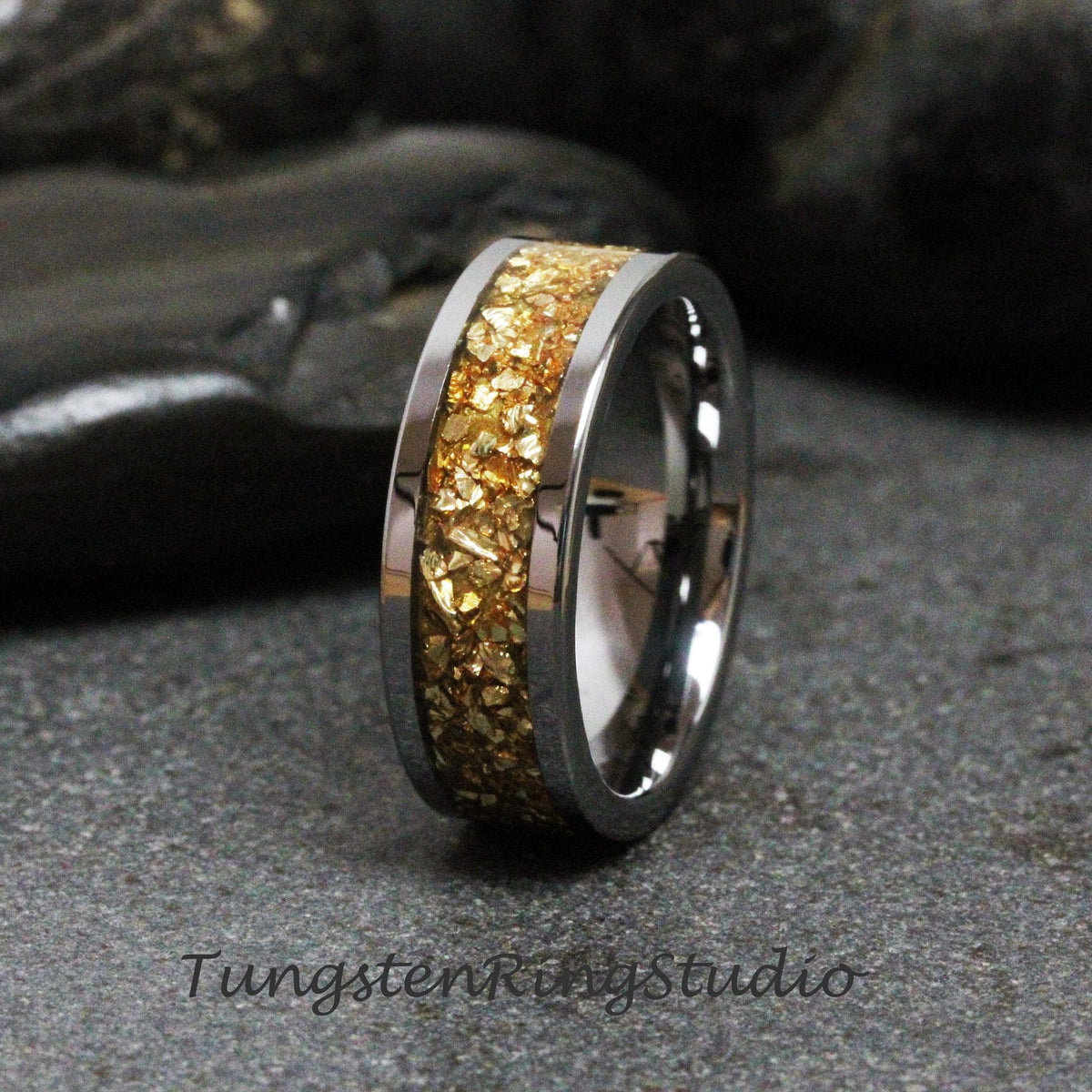 May include: A tungsten carbide ring with a gold inlay. The inlay is made of small gold flakes that are embedded in the ring. The ring is a classic style with a polished finish.