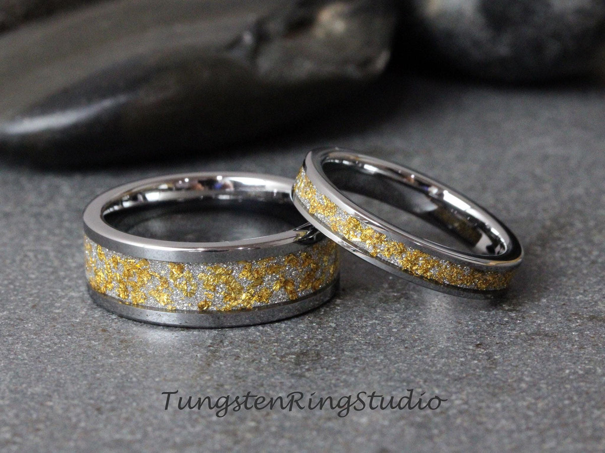 May include: A pair of tungsten wedding bands with a silver and gold inlay. The bands are both polished and have a smooth finish.