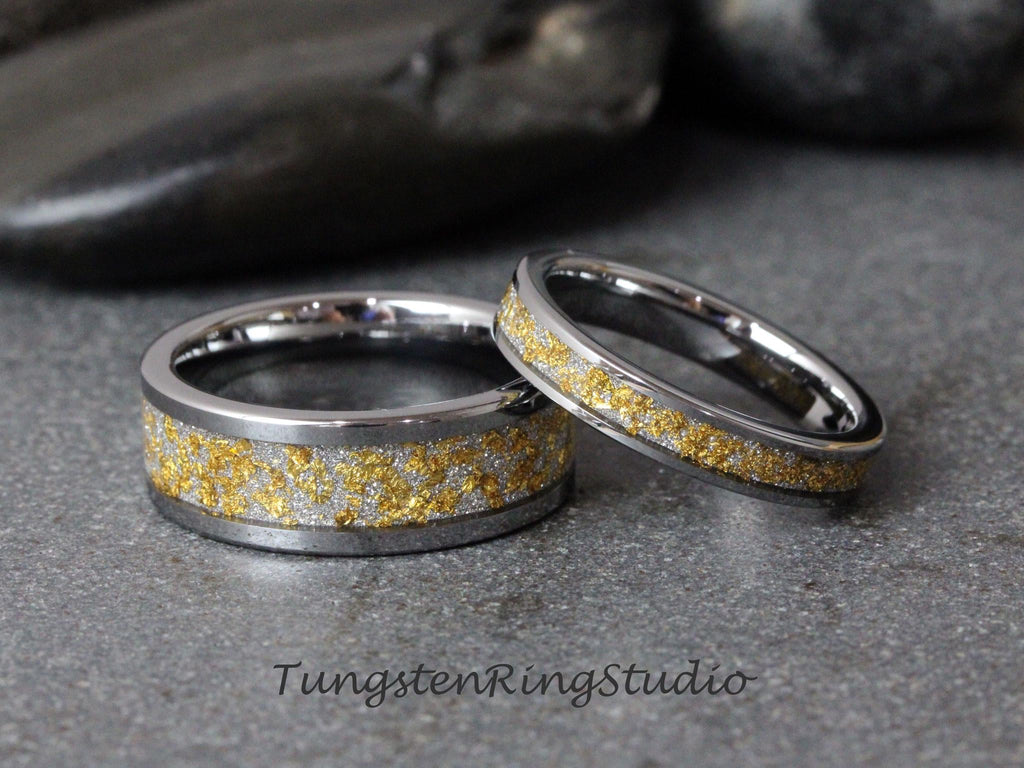 May include: A pair of tungsten wedding bands with a silver and gold inlay. The bands are both polished and have a smooth finish.
