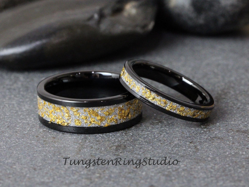 May include: Two black tungsten carbide wedding bands with a gold and silver inlay. The bands are both polished and have a smooth finish.