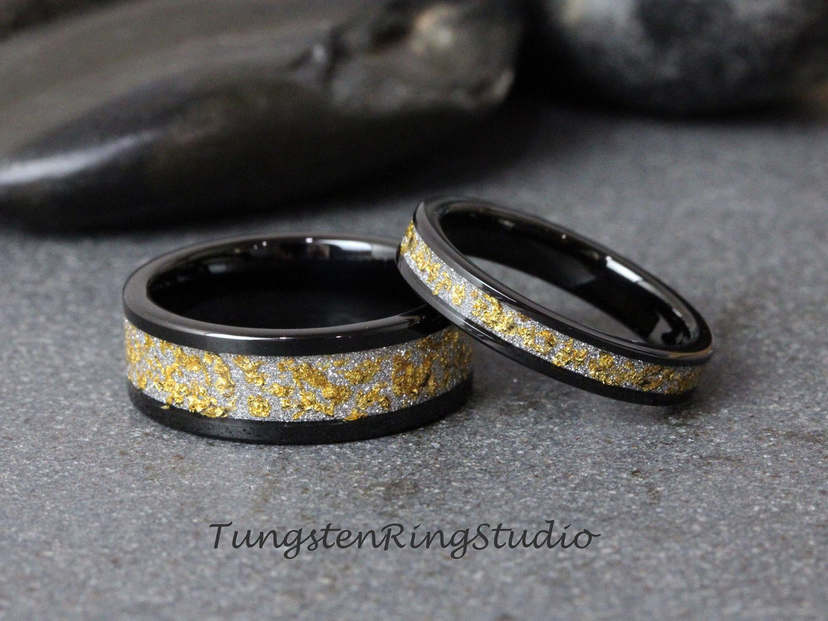 May include: Two black tungsten carbide wedding bands with a gold and silver inlay. The bands are both polished and have a smooth finish.