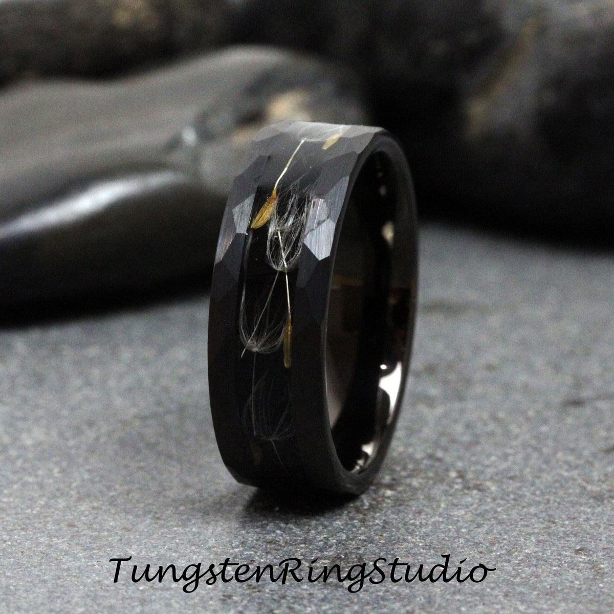 May include: A black tungsten carbide ring with a hammered finish and a band of dandelion seeds embedded in the metal.