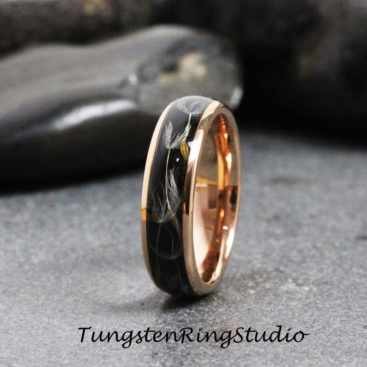 May include: A rose gold tungsten carbide ring with a black inlay featuring a design of dandelion seeds. The ring is a popular choice for wedding bands.