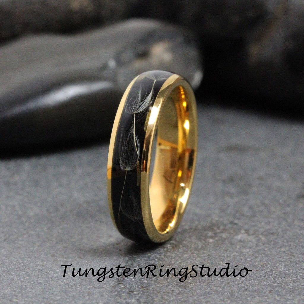 May include: A black tungsten ring with a gold band and a design of dandelion seeds inside. The ring is a wedding band.