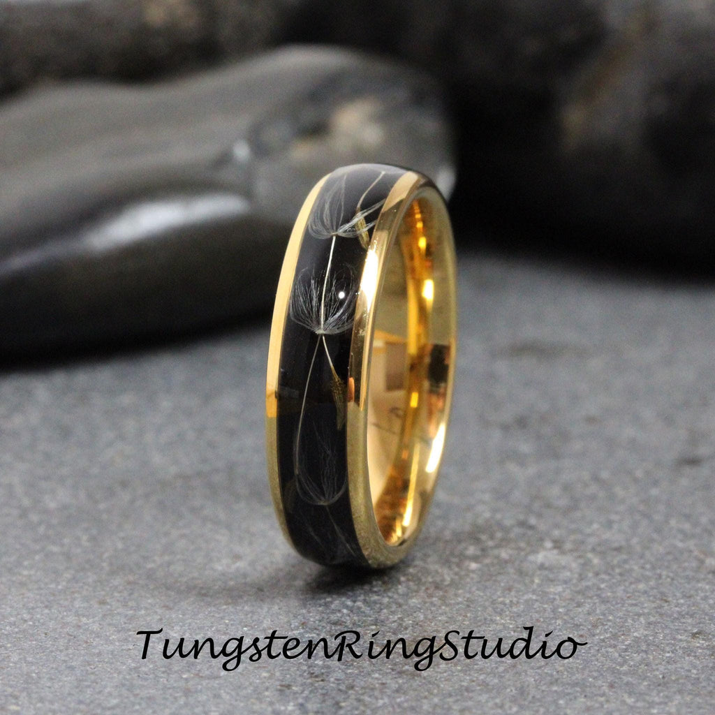 May include: A black tungsten ring with a gold band and a design of dandelion seeds inside the band.