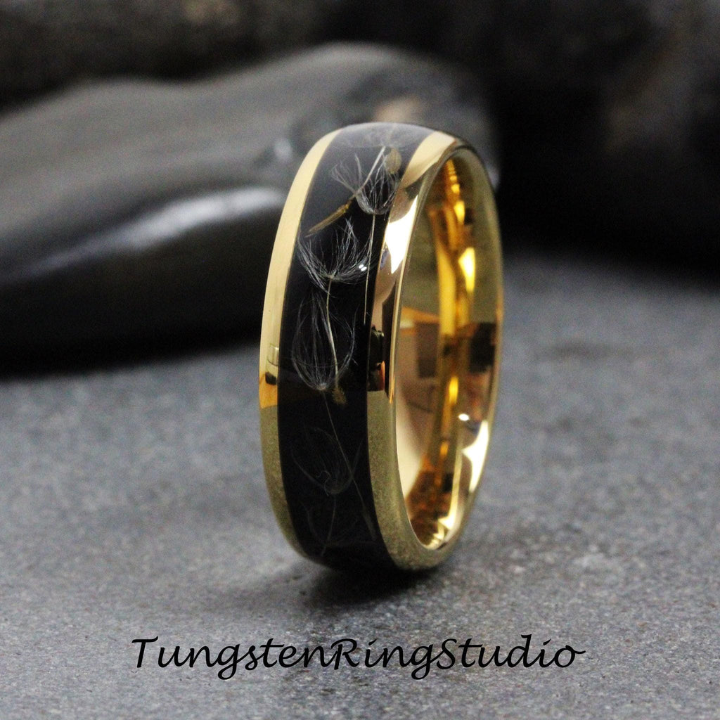 May include: A black tungsten ring with a gold band and a dandelion design. The ring is a wedding band.