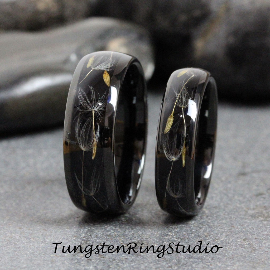 May include: Two black tungsten carbide rings with a dandelion design embedded in the band. The rings are polished and have a high shine.