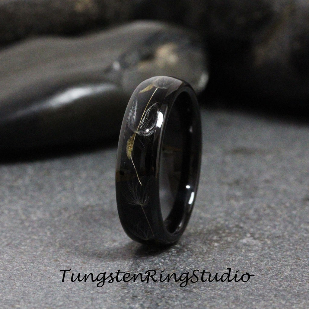 May include: A black tungsten carbide ring with a dandelion design engraved into the band. The ring is polished to a high shine.