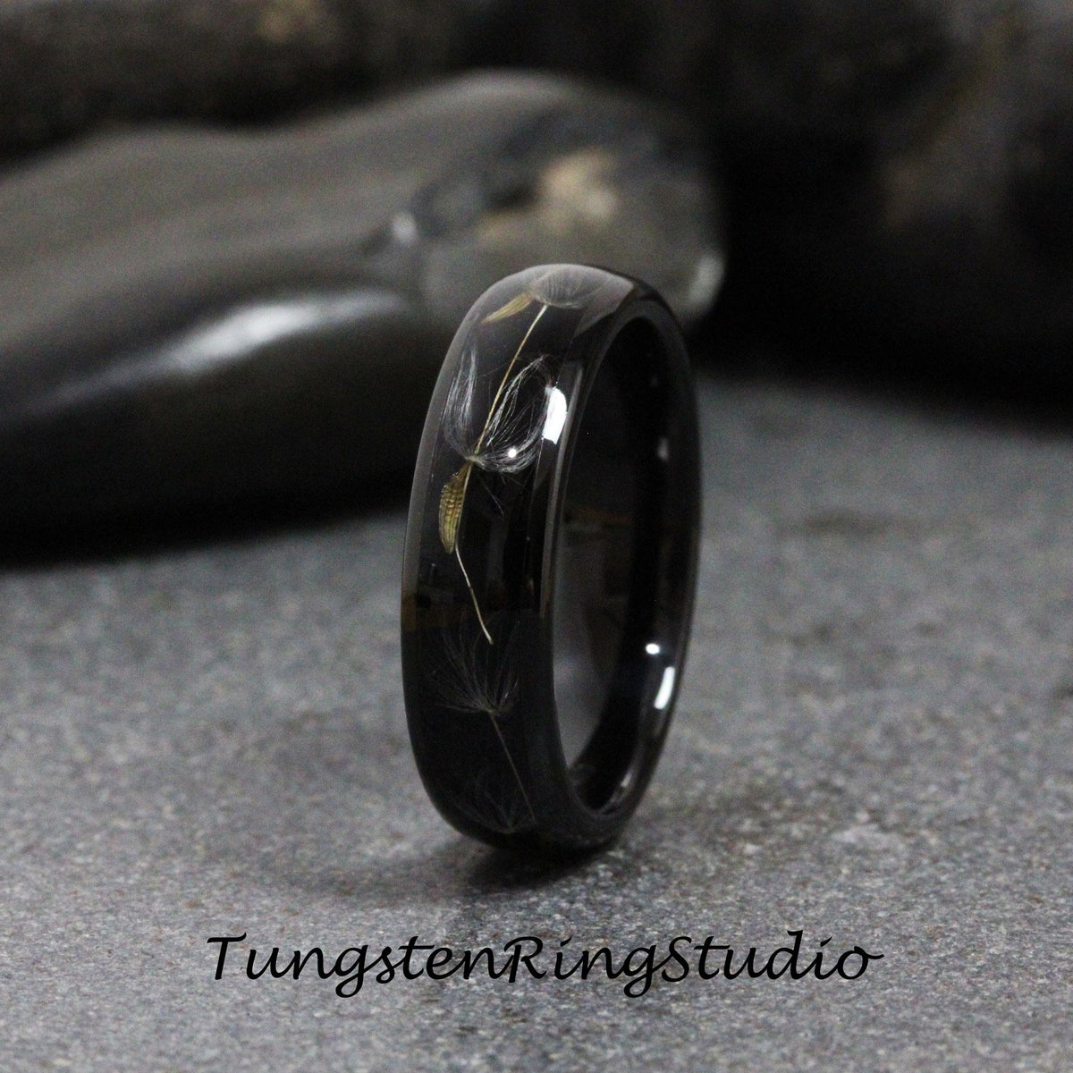 May include: A black tungsten carbide ring with a dandelion design engraved into the band. The ring is polished to a high shine.