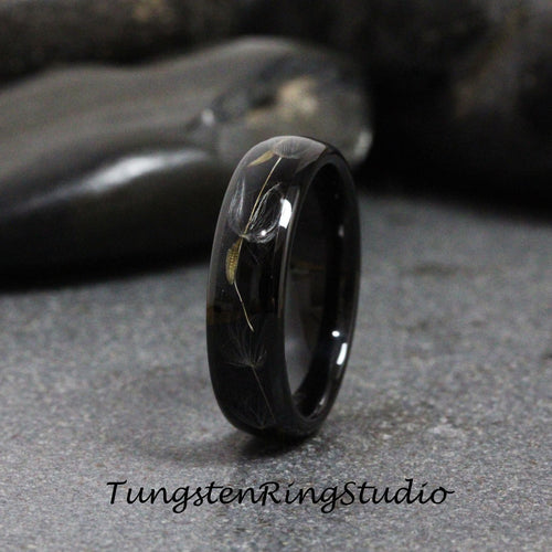 May include: A black tungsten carbide ring with a dandelion design engraved into the band. The ring is polished to a high shine.