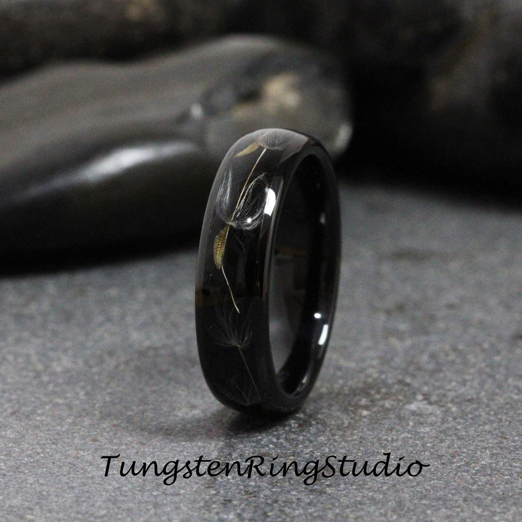 May include: A black tungsten carbide ring with a dandelion design engraved into the band. The ring is polished to a high shine.