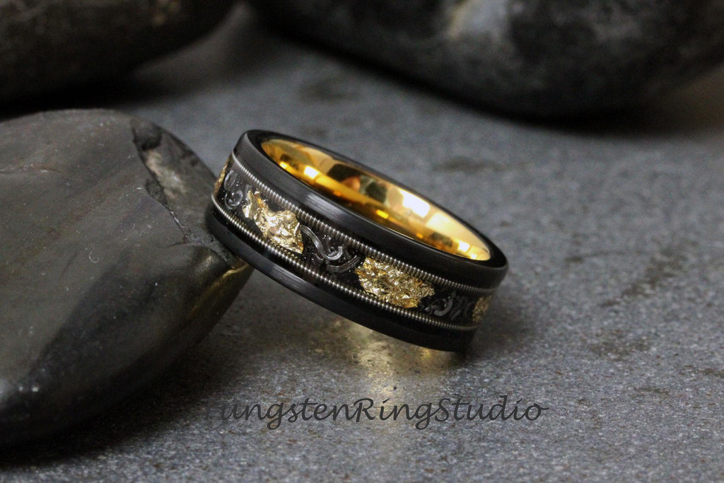May include: A black tungsten carbide ring with a gold inlay and intricate design. The ring has a polished finish and is set against a gray background.