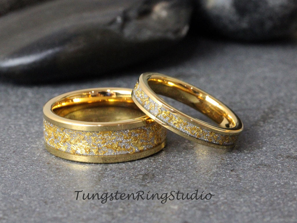 May include: Two gold tungsten carbide wedding bands with a silver speckled finish. The bands are stacked on top of each other.