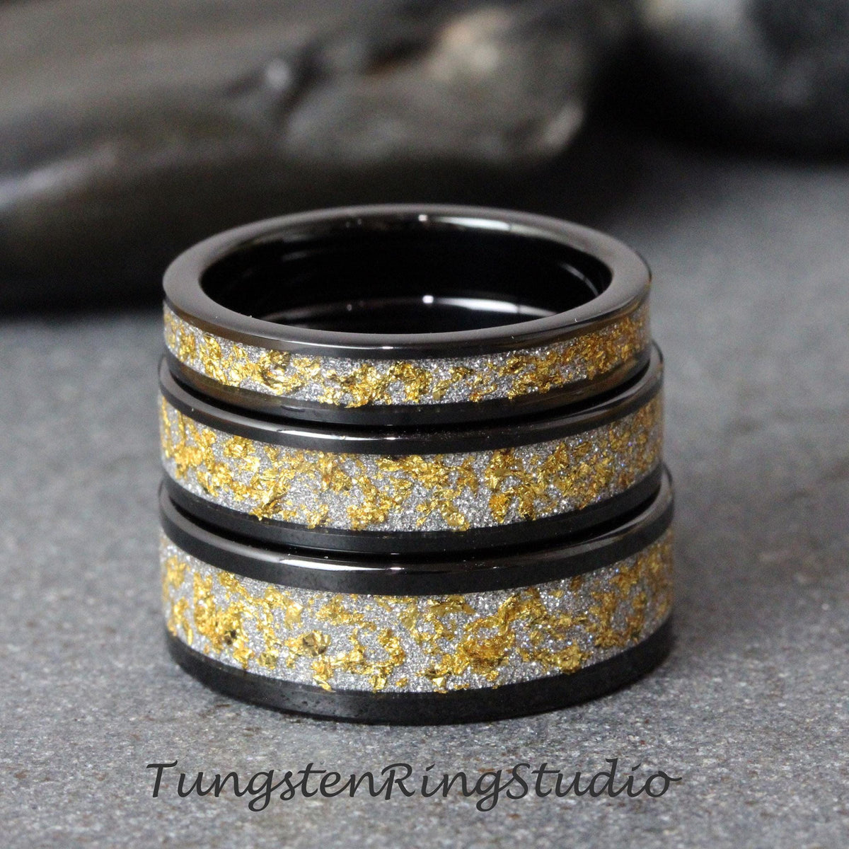 May include: Three black tungsten carbide rings with a gold and silver inlay. The rings are stacked on top of each other.