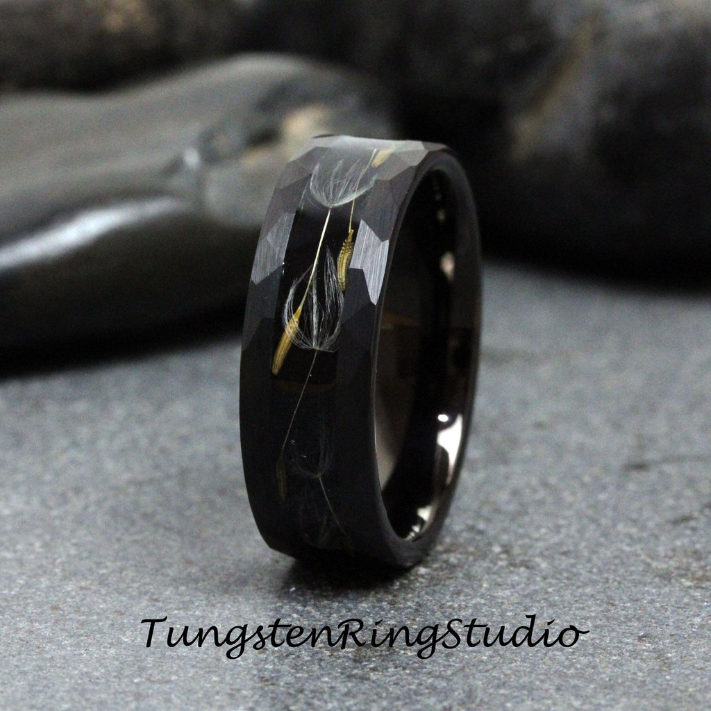 May include: A black tungsten carbide ring with a brushed finish and a design of dandelion seeds embedded in the band.